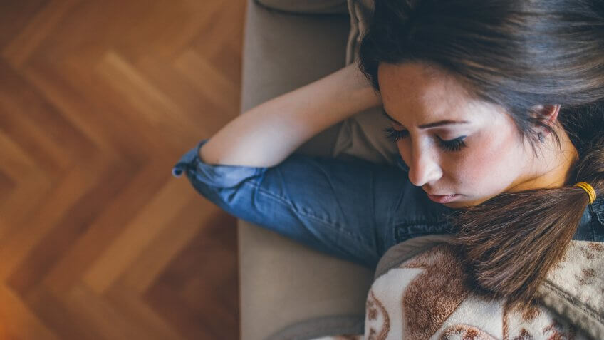 Sleeping woman in high angle view lying on sofa under blanket.