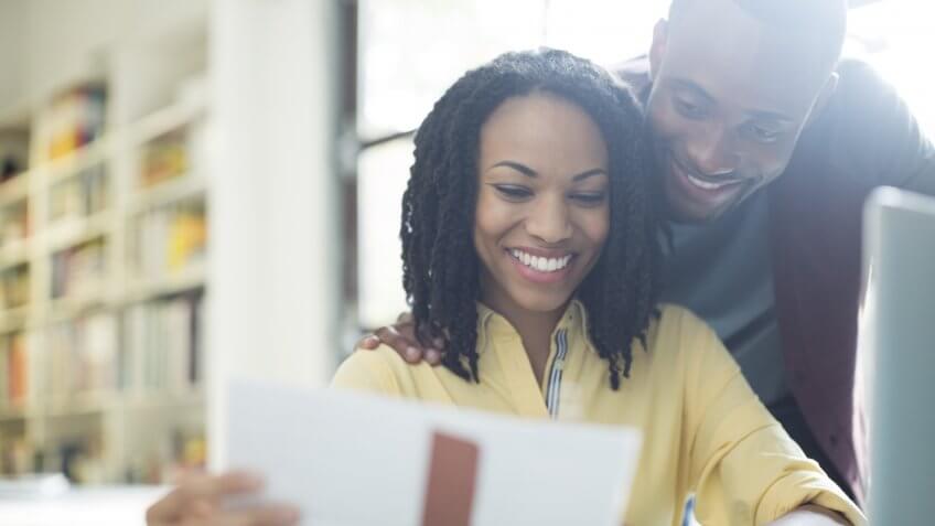 Happy couple reading paperwork at laptop.