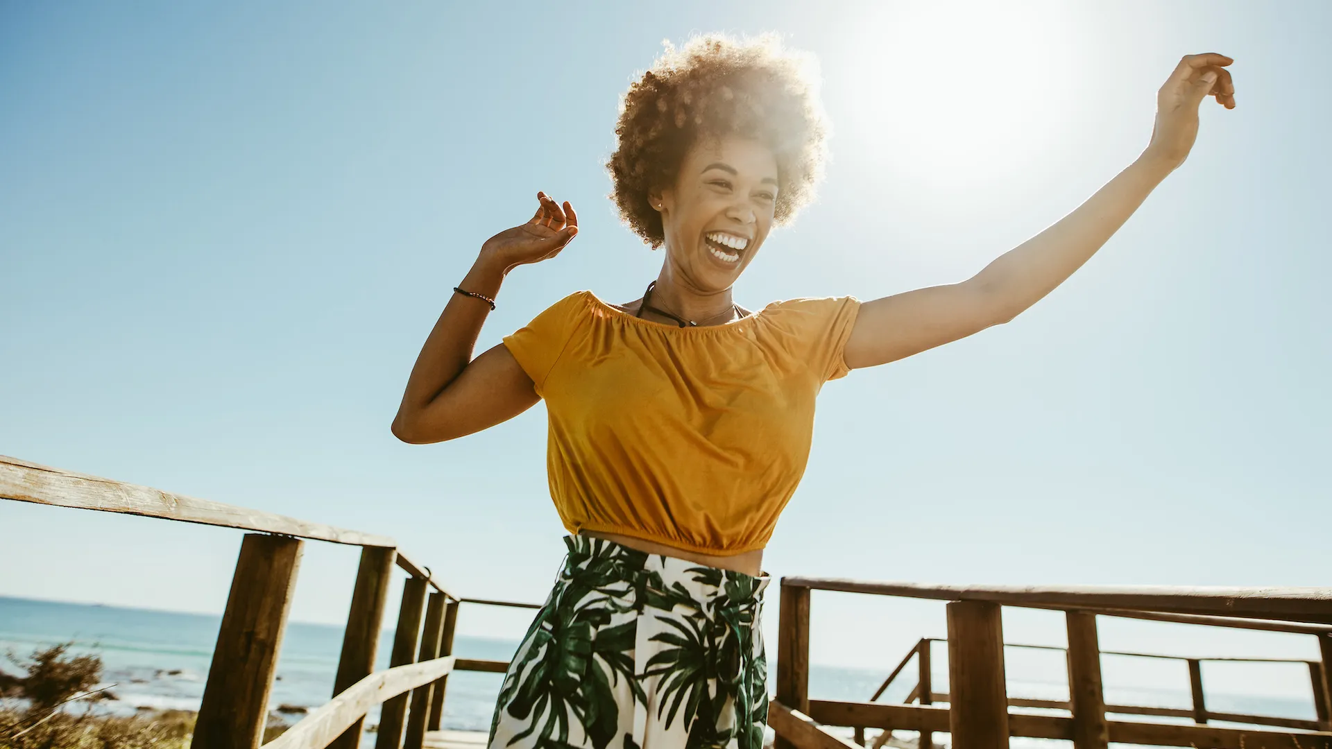 Excited young woman running on a boardwalk with her hands raised on a sunny day.