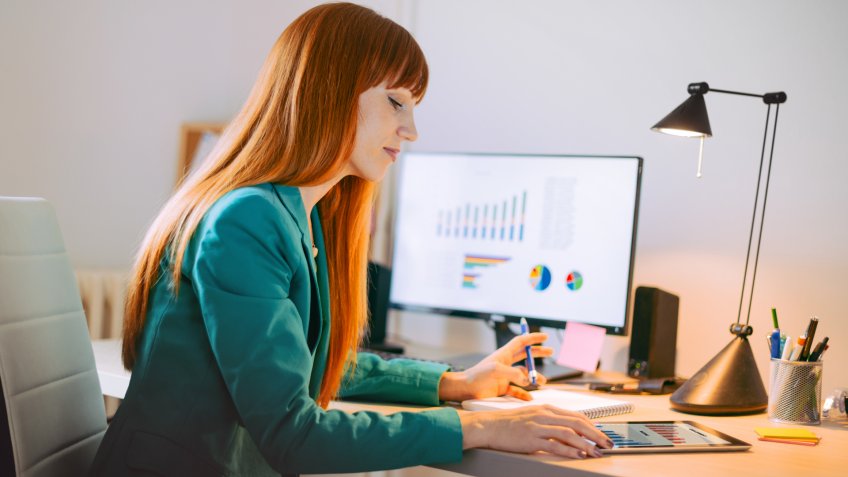 Red head woman working in office and dealing with market financial charts and graphs.