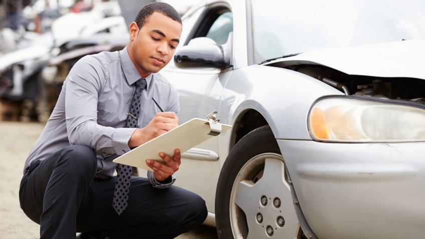 Loss Adjuster Inspecting Car Involved In Accident Crouching Down.