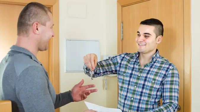 Two adult men standing at doorway with keys and contract.