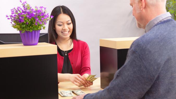 An adult man bank customer making a financial transaction with a bank teller over the counter in a retail bank.