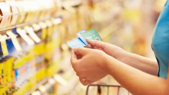 Woman In Grocery Aisle Of Supermarket With Coupons.