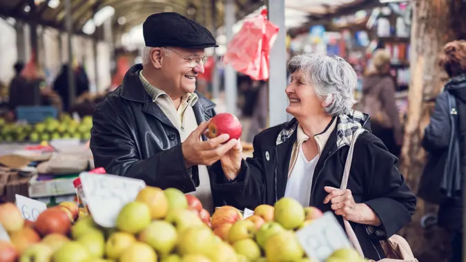 Happy senior man and woman choosing apples to buy at market stall.