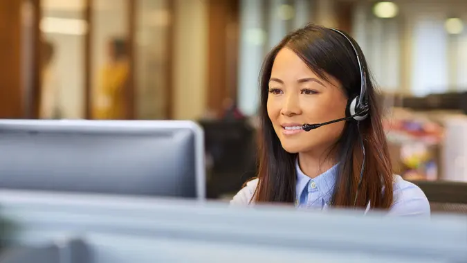 a young call centre representative greets a caller in a large open plan office .