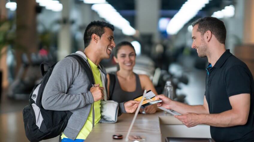 Happy couple of people at the gym talking to the receptionist about membership plans - healthy lifestyle concepts.