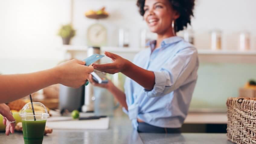 Cropped shot of female employee taking payment from customer, focus on female hands giving credit card for juice bar payment.