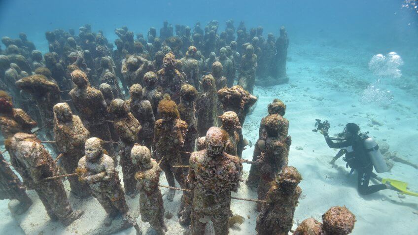 High angle view scuba diver photographing Cancuns underwater statues, Isla Mujeres, Quintana Roo, Mexico.