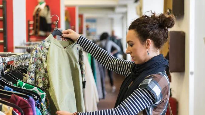 A woman shopping at a thrift store -- holding up a shirt that she is considering buying.