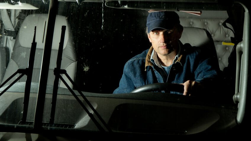 A long haul truck driver in his semi lit up by oncoming headlights.