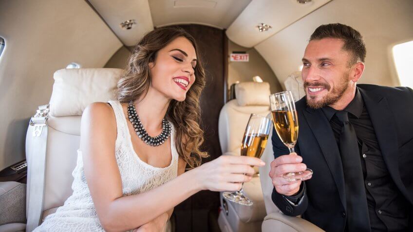 Business couple sitting inside private jet airplane and having a champagne toast.