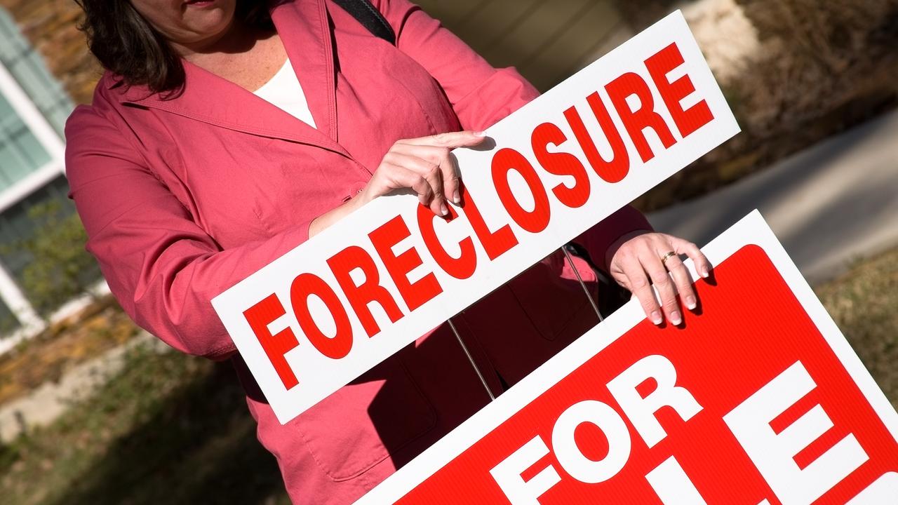 Realtor placing a foreclosure sign on the for sale sign in front of a home.