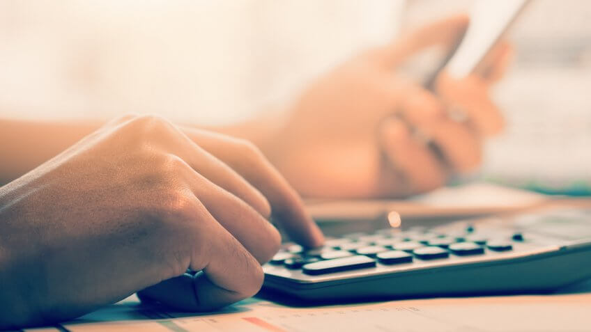 Close up business man hand holding smartphone and doing finance and calculate on wooden table about cost at home office.
