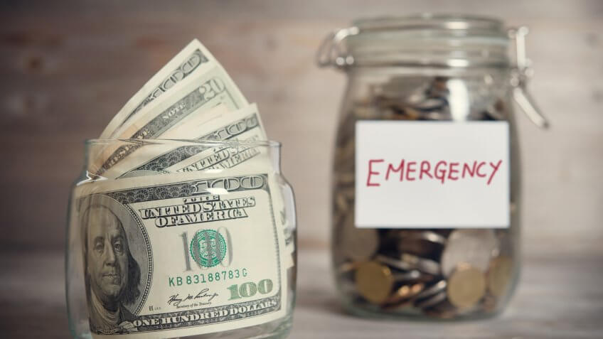 Dollars and coins in glass jar with emergency label, financial concept.