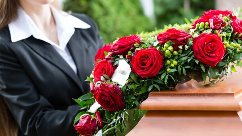Mourning woman on funeral with red rose standing at casket or coffin.