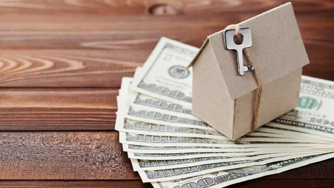 Model of cardboard house with key and dollar money.