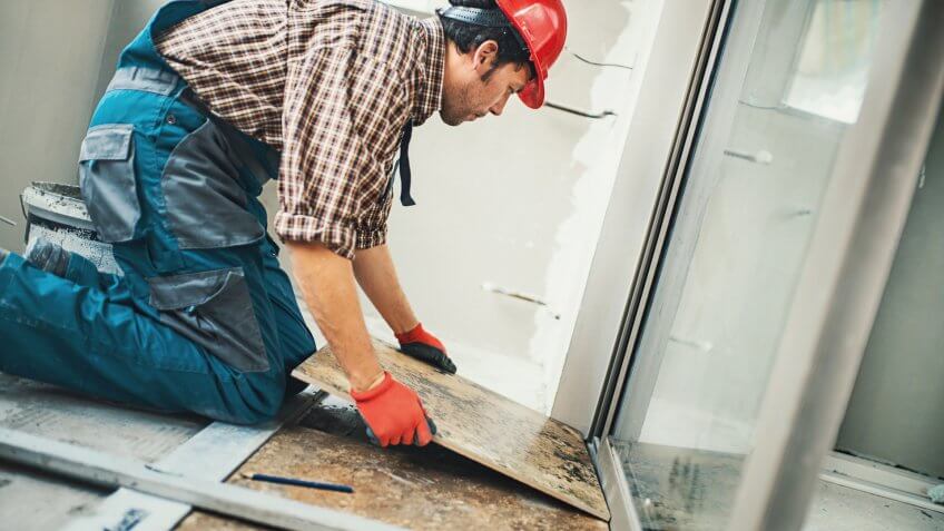 Closeup side view of a handyman installing green ceramic tiles over apartment floor.