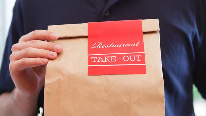 Close-up of an unidentifiable delivery man holding a take out food brown paper bag of restaurant dinner, delivering the fast food meal package.