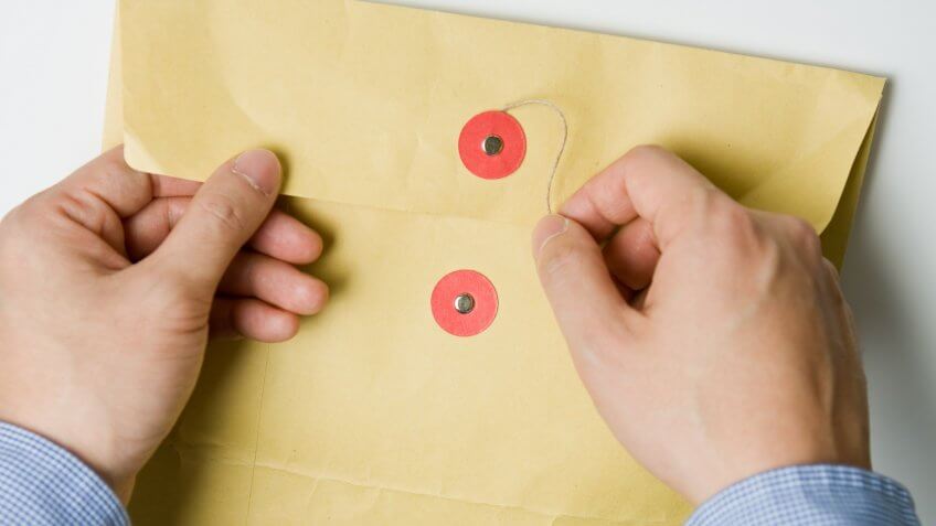 Person opening a confidential official document in an envelope.