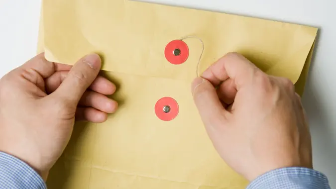 Person opening a confidential official document in an envelope.