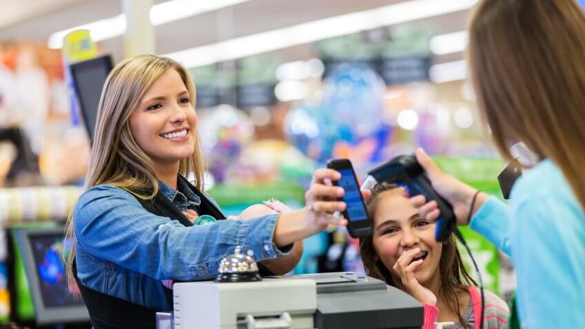 Mid adult Caucasian woman is using her smart phone app to pay for groceries in local grocery store.