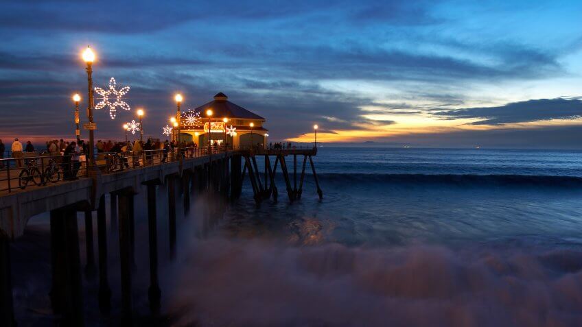 People watching huge waves from the pier at sunset in Huntington Beach, CA.