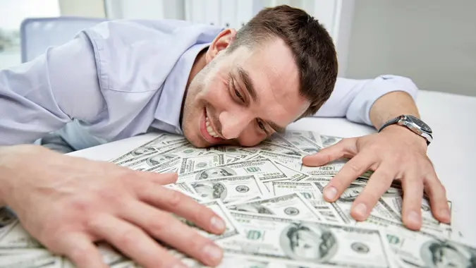 business, people, success and fortune concept - happy businessman with heap of dollar money in office.