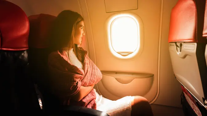 Young beautiful woman sit by window of airplane during flight.