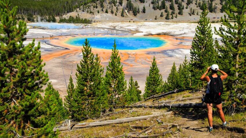 A hiker looking down on Yellowstone National Park's Grand Prismatic Spring in Yellowstone National Park, the largest hot spring in the United States, and the third largest in the world.