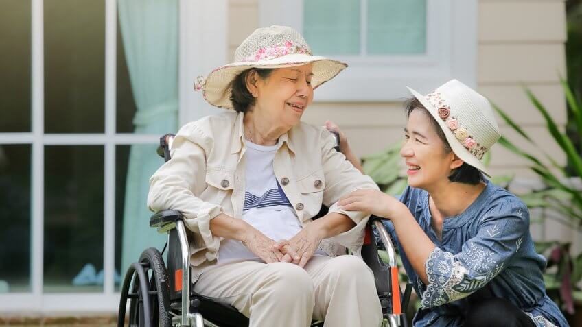 Elderly woman relax on wheelchair in backyard with daughter.