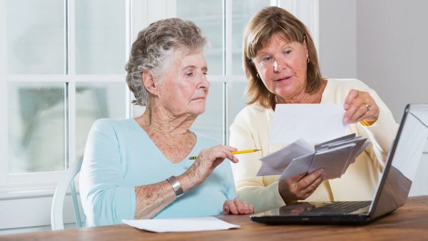 Mature woman (60s) helping elderly mother (90s) pay bills.