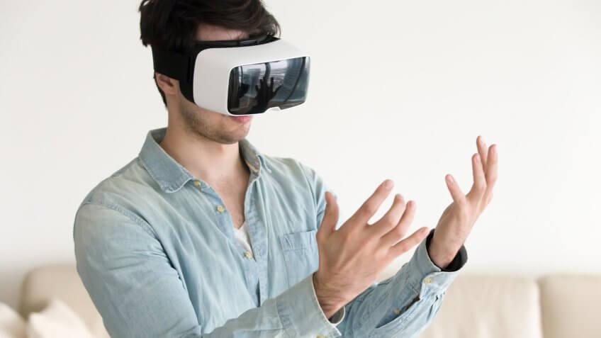 Trying VR headset for the first time at home, young guy looking at his hands wearing virtual reality glasses, innovative future realistic technology for mobile apps and gaming.