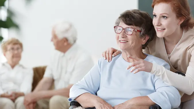 Assistant shows something to the patient on wheelchair in senior home.