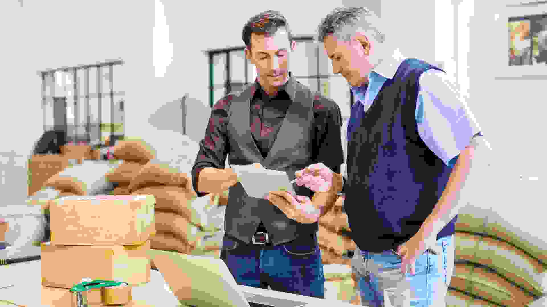Two business men working at coffee storage room and looking at digital tablet.