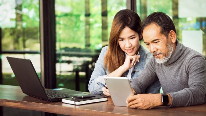 Smiling mature man with white stylish short beard using tablet with charming woman teenage.