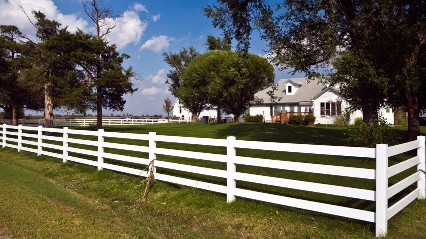 White rail fence surrounds tidy farmhouse in Kansas.