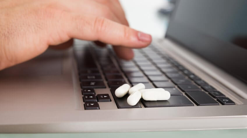 Close-up Of Person's Hand Using Laptop With Pills Over Keypad.
