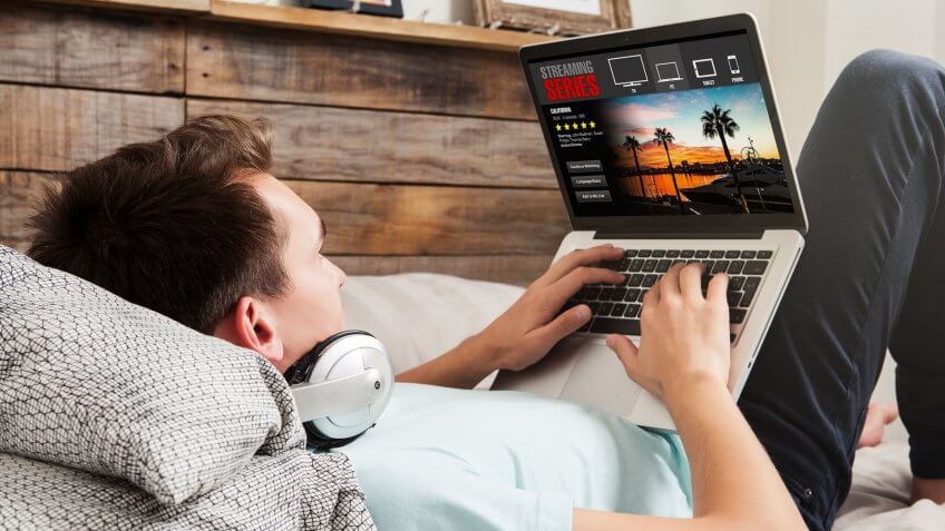 Man watching streaming series in a laptop computer, lying in the bed.