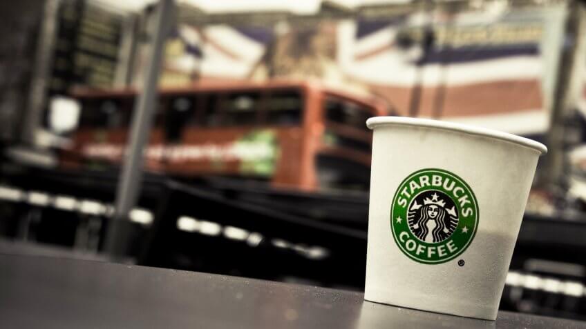 LONDON, UK - OCTOBER 13, 2009 - A Starbucks paper coffee cup on a table in Camden Town, London bus and Union Jack on background.