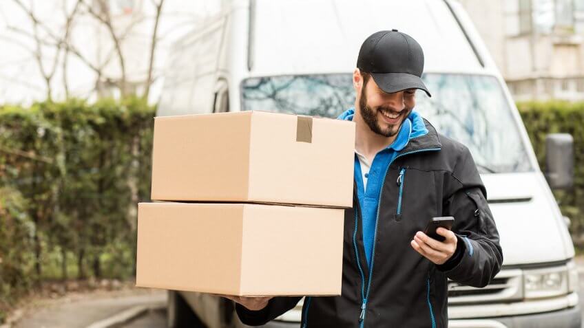 delivery man holding boxes checking smartphone