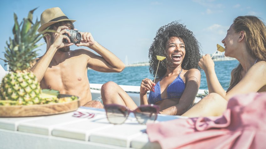 Happy friends having fun and eating fresh pineapple fruit at boat party - Young people taking photos in caribbean sea tour - Youth, tropical, travel and summer vacation concept - Focus on black girl.
