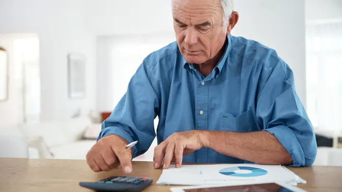 senior man using a calculator while reviewing his budget