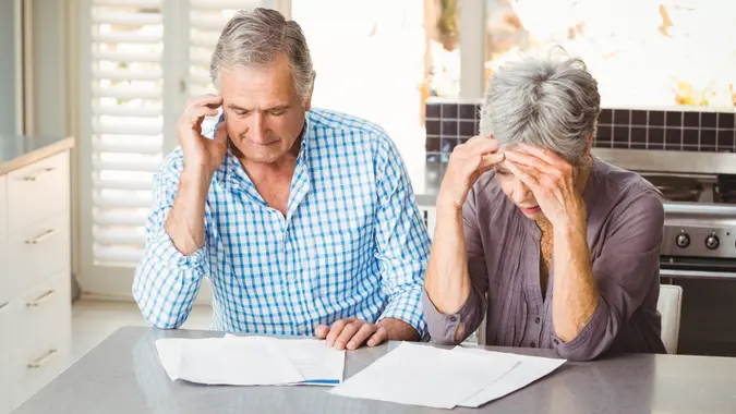 Worried senior couple with documents sitting in kitchen at home.