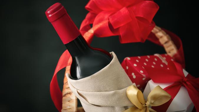 Wine bottle with gift boxes in wicker basket on dark background.
