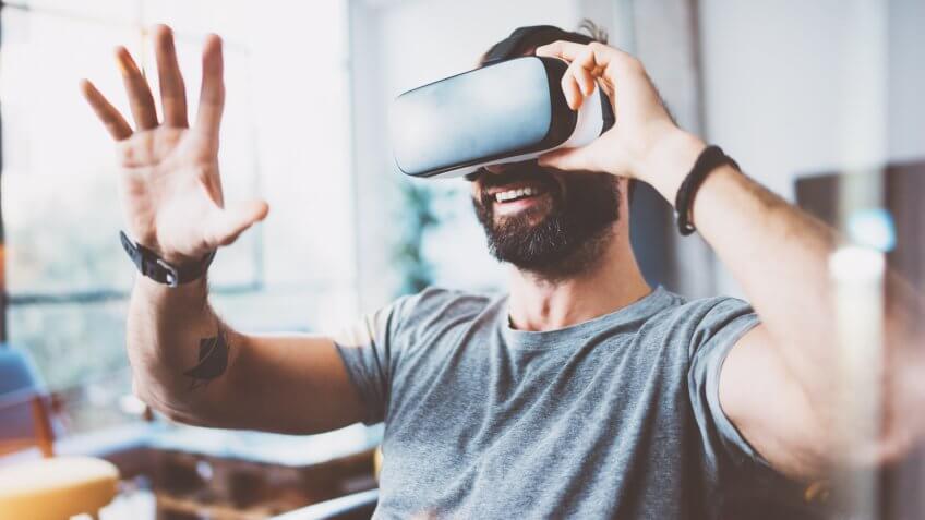 Young bearded man wearing virtual reality glasses in modern interior design coworking studio.