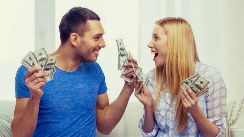 love, family, finance, money and happiness concpet - smiling couple with money and piggybank ot table at home.