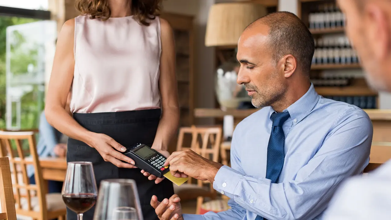 Waiter holding credit card swipe machine while customer typing code.