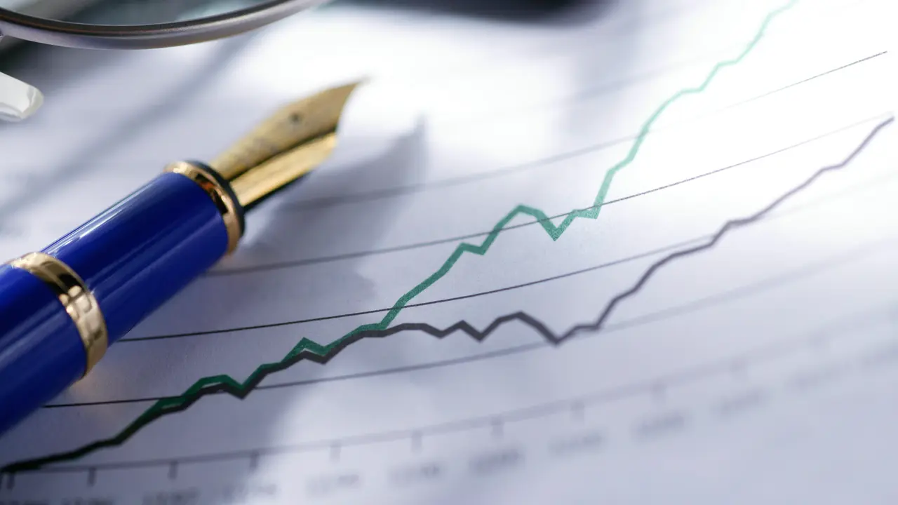 A blue and gold fountain pen and a pair of eyeglasses sit on top of a chart showing diverging trend in sales growth or stock market performance.