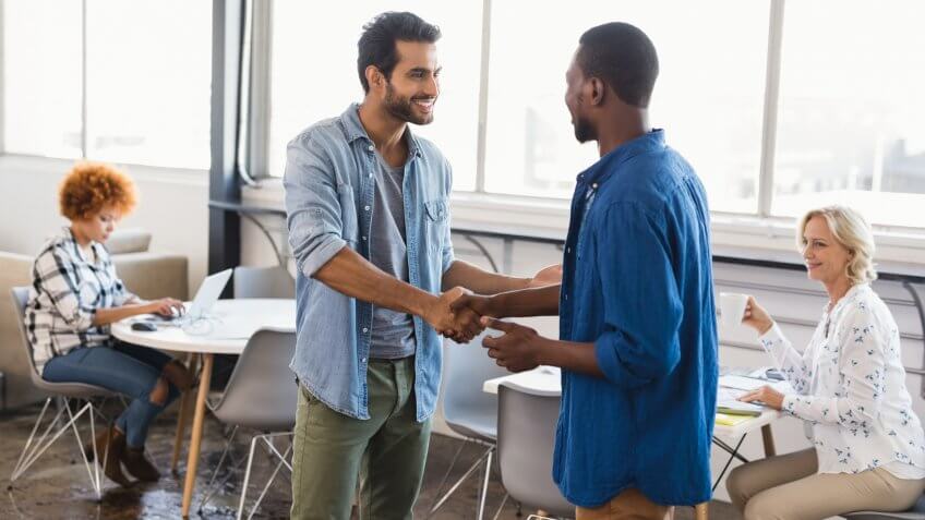 Happy young male business people shaking hands at creative office.